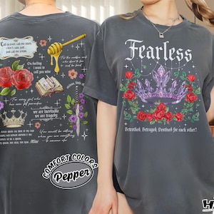 Może przedstawiać: Ciemnoszare koszulki z grafikami. Jedna koszulka ma koronę, róże i napis "Fearless". Druga koszulka ma róże, koronę, nabierak do miodu i tekst. Obie koszulki mają markę Comfort Colors.