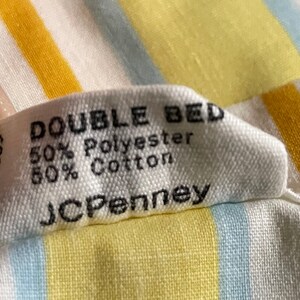 May include: A white tag with black text that reads "DOUBLE BED 50% Polyester 50% Cotton JCPenney" on a yellow and blue striped fabric.