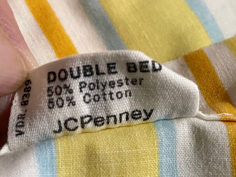 May include: A white tag with black text that reads "DOUBLE BED 50% Polyester 50% Cotton JCPenney" on a yellow and blue striped fabric.