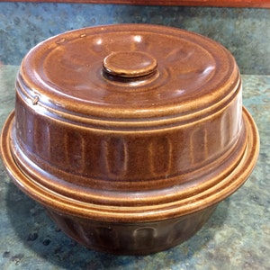 May include: A brown ceramic casserole dish with a lid. The dish has a fluted design and the lid has a knob on top.