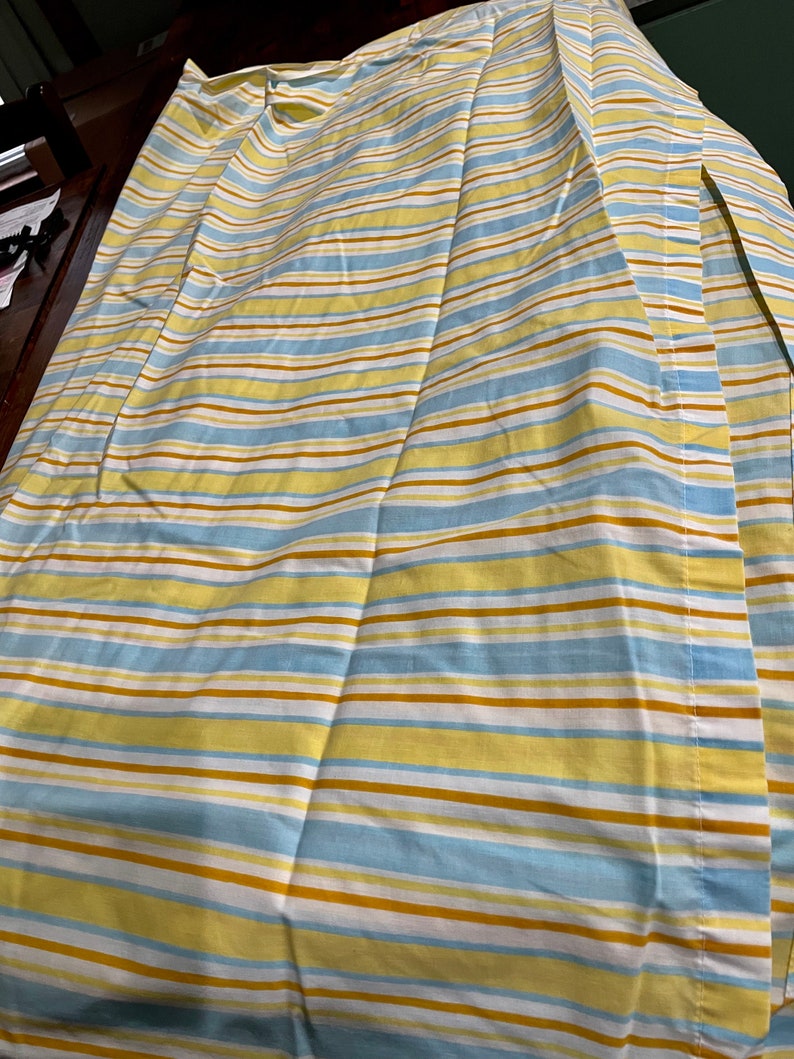 May include: A striped fabric with yellow, blue, and brown stripes. The fabric is folded in half and has a seam down the center.