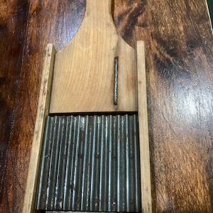 May include: A vintage wooden and metal potato ricer with a handle. The ricer has a corrugated metal surface and is made of wood.