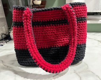 May include: A crocheted tote bag with red and black stripes. The bag has two thick red straps.