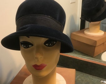 May include: A dark blue felt cloche hat with a black grosgrain ribbon band. The hat is on a mannequin head.