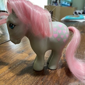 May include: A gray My Little Pony with pink hair and tail. The pony has pink hearts on its flank.