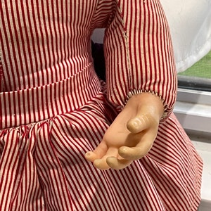 Puede incluir: Una mu&ntilde;eca vintage con un vestido a rayas rojas y blancas. La mu&ntilde;eca tiene cabeza y manos de porcelana.
