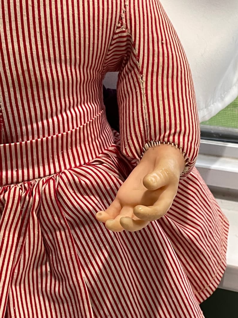 Puede incluir: Una mu&ntilde;eca vintage con un vestido a rayas rojas y blancas. La mu&ntilde;eca tiene cabeza y manos de porcelana.