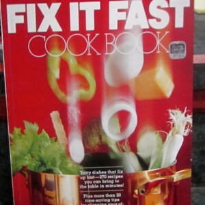 May include: A red cookbook with the title "Fix It Fast Cookbook" by Better Homes and Gardens. The cover features a copper pot with vegetables and herbs.