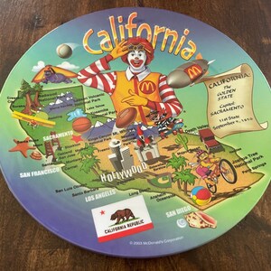 May include: A colorful, round decorative plate featuring a map of California with illustrations of landmarks and Ronald McDonald. The plate includes the text "California" and "California Republic".