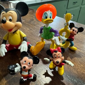 May include: A collection of vintage Disney character figurines, including Mickey Mouse, Minnie Mouse, Donald Duck, and Goofy. The figurines are made of plastic and are in good condition.