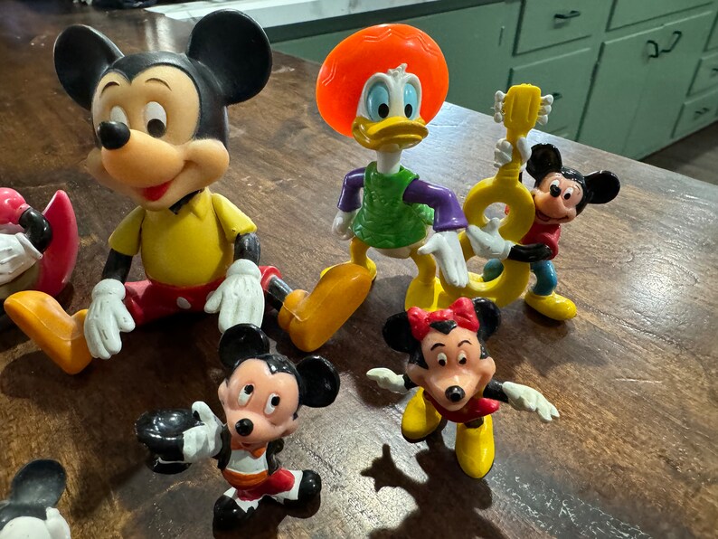 May include: A collection of vintage Disney character figurines, including Mickey Mouse, Minnie Mouse, Donald Duck, and Goofy. The figurines are made of plastic and are in good condition.