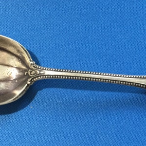 May include: A silver spoon with a rounded, pointed bowl and an ornate handle. The bowl is engraved with the words "Bible Class 1910".