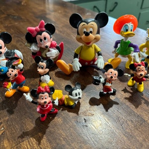 May include: A collection of nine vintage Disney character figurines, including Mickey Mouse, Minnie Mouse, Donald Duck, and Goofy. The figurines are made of plastic and are painted in bright colors. They are all in good condition and would make a great addition to any Disney fan's collection.