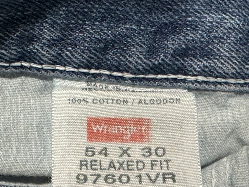 May include: A white tag with black text that reads "Made in", "100% Cotton / Algodon", "Wrangler", "54 X 30", "Relaxed Fit", and "97601VR".