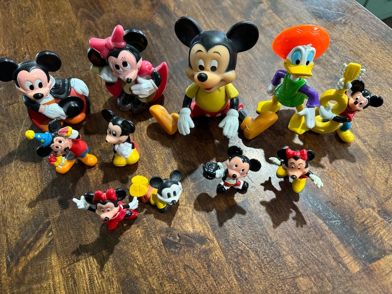 May include: A collection of ten small plastic Disney character figurines, including Mickey Mouse, Minnie Mouse, Donald Duck, and Goofy. The figurines are all in various poses and are painted in bright colors.