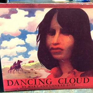 May include: A book cover with a watercolor illustration of a woman with long dark hair and a red shirt. The background is a blue sky with white clouds. The title of the book is "Dancing Cloud" by Mary and Conrad Buff.