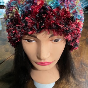 May include: A colorful, fuzzy headband with red, blue, green, and purple yarn. The headband is on a mannequin head with long black hair.