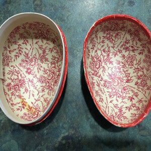 May include: Two red and white paper egg-shaped containers with a floral pattern. The text on the bottom of the containers reads "container made in Western Germany".
