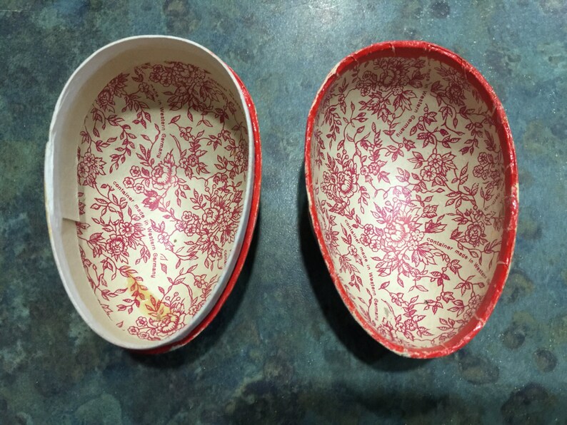 May include: Two red and white paper egg-shaped containers with a floral pattern. The text on the bottom of the containers reads "container made in Western Germany".