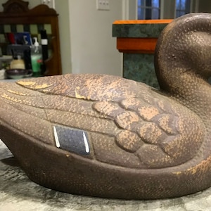 Puede incluir: Un señuelo de pato de madera marrón y beige con una mancha de ala azul y blanca. El señuelo tiene un aspecto realista con una cabeza y un pico detallados.