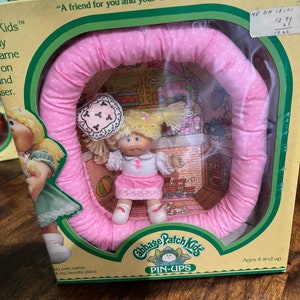 May include: A pink and white Cabbage Patch Kids Pin-Ups playset with a doll and a pink ring. The box has the text "A friend for you and your Cabbage Patch Kid." and "Ages 4 and up."
