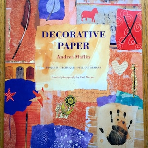 May include: A book cover with a colorful collage of paper scraps. The title is "Decorative Paper" by Andrea Maflin. The book features projects, techniques, and pull-out designs.
