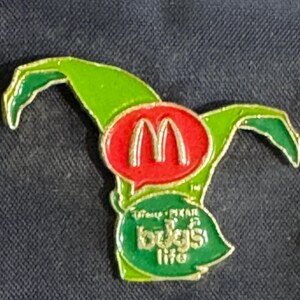 May include: Green and red pin with a speech bubble containing the McDonald's logo and the text "Enjoy the life" in a green speech bubble.