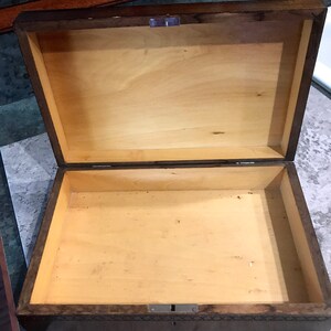 May include: A wooden box with a hinged lid and a lock. The box is made of dark wood with a light wood interior. The box is empty.