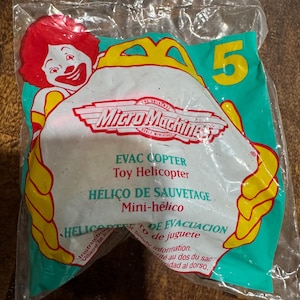 May include: Sealed Micro Machines toy helicopter in a plastic bag. The packaging features a cartoon clown, the number 5, and text in multiple languages including "EVAC COPTER" and "Toy Helicopter."