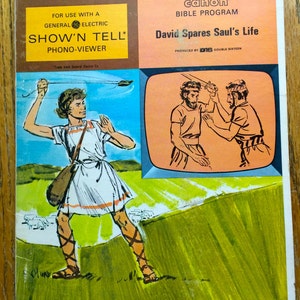 Puede incluir: Una ilustración vintage de una escena de la historia bíblica de David y Goliat. La ilustración muestra a David, un joven pastor, enfrentándose a Goliat, un guerrero gigante. La ilustración es de un visor de fonógrafo "Show 'n Tell", un producto para que los niños aprendan sobre la Biblia. El texto de la portada dice "David perdona la vida de Saúl" y "Programa bíblico Canon".