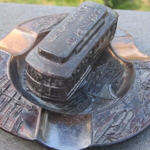 May include: A vintage metal ashtray featuring a detailed depiction of a San Francisco streetcar. The ashtray is decorated with the words "San Francisco, Calif. No. 2400, 1923" on the top of the streetcar. The ashtray is a great collectible for fans of San Francisco.