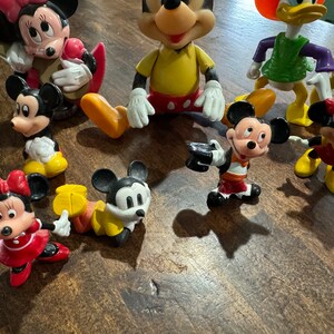 May include: A collection of vintage Disney character figurines, including Mickey Mouse, Minnie Mouse, Donald Duck, and Goofy. The figurines are made of plastic and are painted in bright colors.