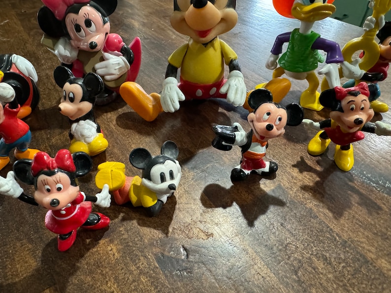 May include: A collection of vintage Disney character figurines, including Mickey Mouse, Minnie Mouse, Donald Duck, and Goofy. The figurines are made of plastic and are painted in bright colors.