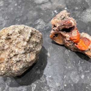 May include: Two natural rock formations, one is a round, light brown geode with a rough surface, the other is a smaller, irregularly shaped rock with red and white layers.