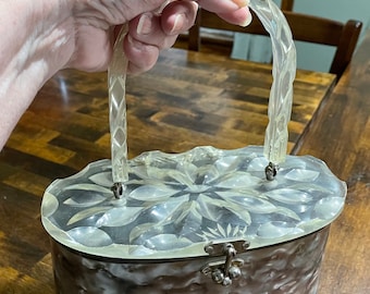 Könnte beinhalten: Eine vintage, ovale, durchsichtige Plastiktasche mit Blumenmuster und einem silbernen Verschluss. Die Tasche hat einen durchsichtigen Plastikgriff.