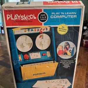 May include: A vintage Playskool Play 'N Learn Computer toy box featuring a blue and yellow plastic computer with two white reels, a red knob, and a yellow storage compartment. The box displays the text Play 'N Learn Computer, ages 3 to 8 years.
