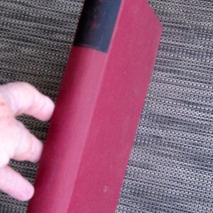 May include: A red hardcover book with a black spine. The title of the book is not visible.
