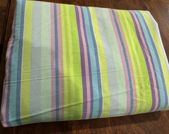 May include: A rectangular fabric piece featuring a vertical striped pattern in shades of lime green, light blue, lavender, and white. The textile displays a repeating sequence of these colors across its entire surface, creating a consistent and balanced visual arrangement of parallel lines throughout the material.