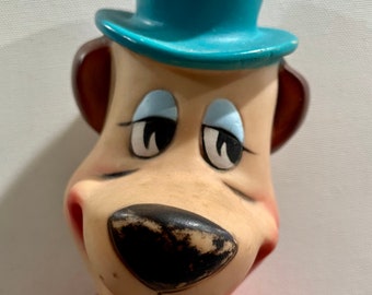 May include: A vintage plush toy of a cartoon bear wearing a blue top hat and a red sweater. The bear has a brown nose and a wide smile.