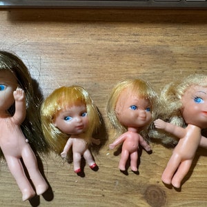 May include: Four small plastic dolls with painted blue eyes and blonde or brown hair. The dolls are nude and have no clothing.