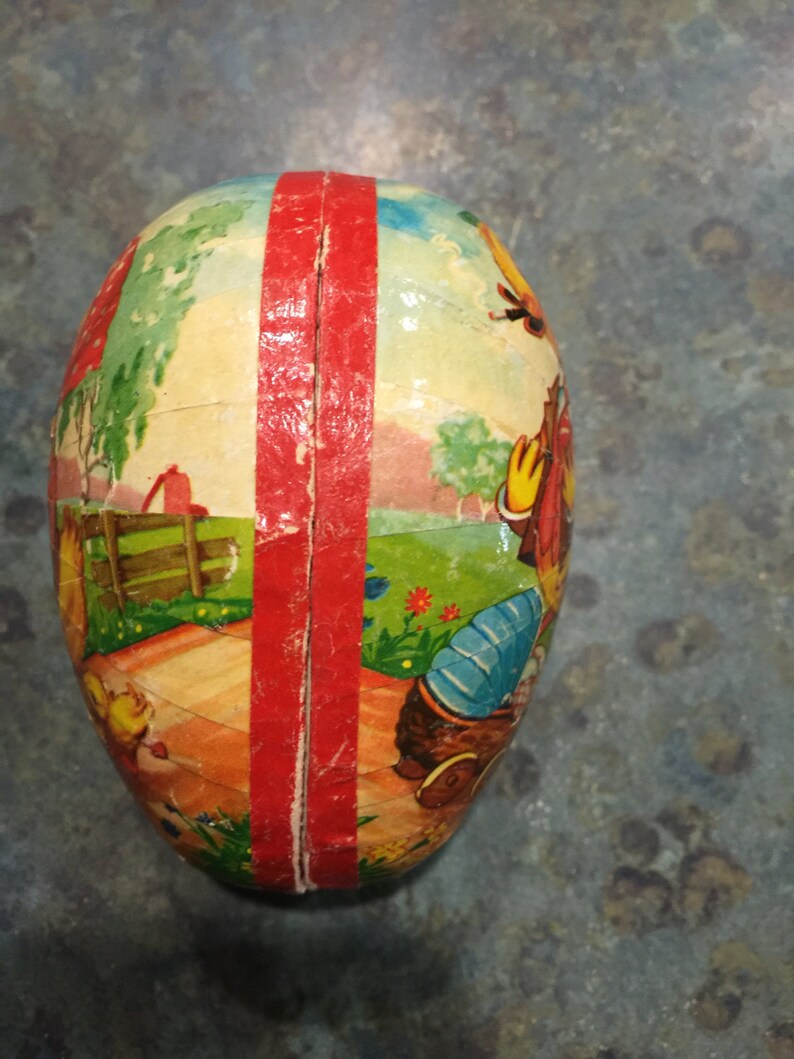May include: A vintage Easter egg made of papier-m&acirc;ch&eacute; with a red stripe down the centre. The egg is decorated with a colourful scene of a farm with a red barn, a fence, and a boy in a blue shirt and red hat.