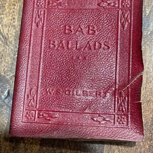 May include: A red leather-bound book with the title "Bab Ballads" and the author's name "W.S. Gilbert" embossed on the cover.