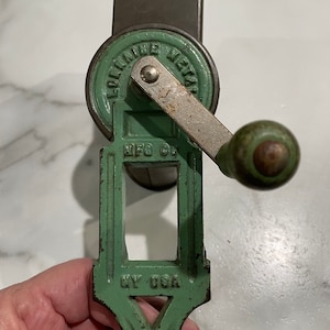 May include: Antique green metal coffee grinder with a crank handle. The grinder has the text "Lorraine Metal Mfg Co NY USA" on it.