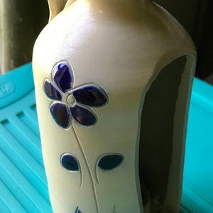 Puede incluir: Una jarra de cer&aacute;mica blanca con un dise&ntilde;o de flor azul. La jarra tiene un asa y un corte en un lado.