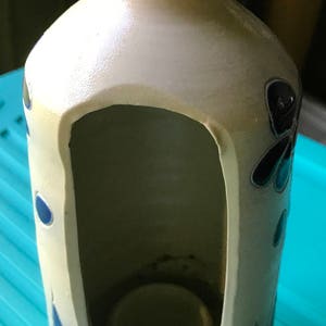 Puede incluir: Un portavelas de cer&aacute;mica blanca con un dise&ntilde;o floral azul y negro. El portavelas tiene un recorte en forma de casa con un peque&ntilde;o portavelas en el interior.