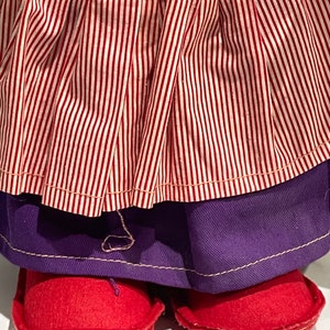 Puede incluir: Una falda de rayas rojas y blancas con una falda interior morada y zapatos de fieltro rojo.