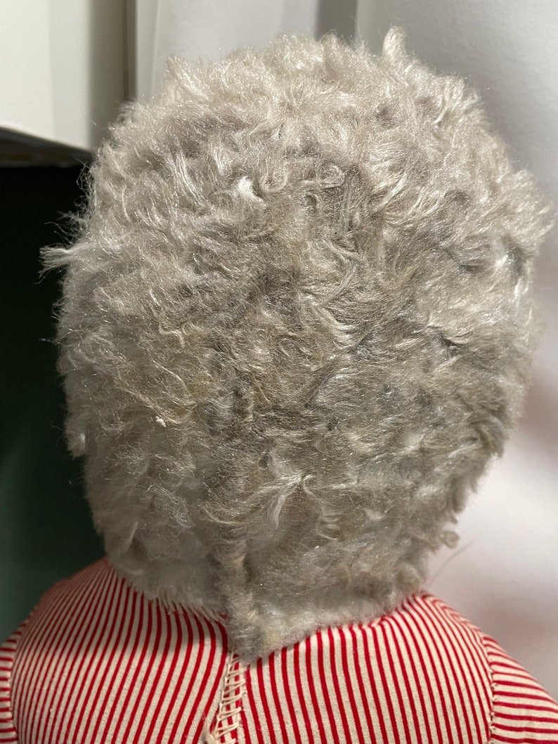 Puede incluir: Una mu&ntilde;eca vintage con una cabeza de mohair gris y esponjosa y un vestido a rayas rojas y blancas.