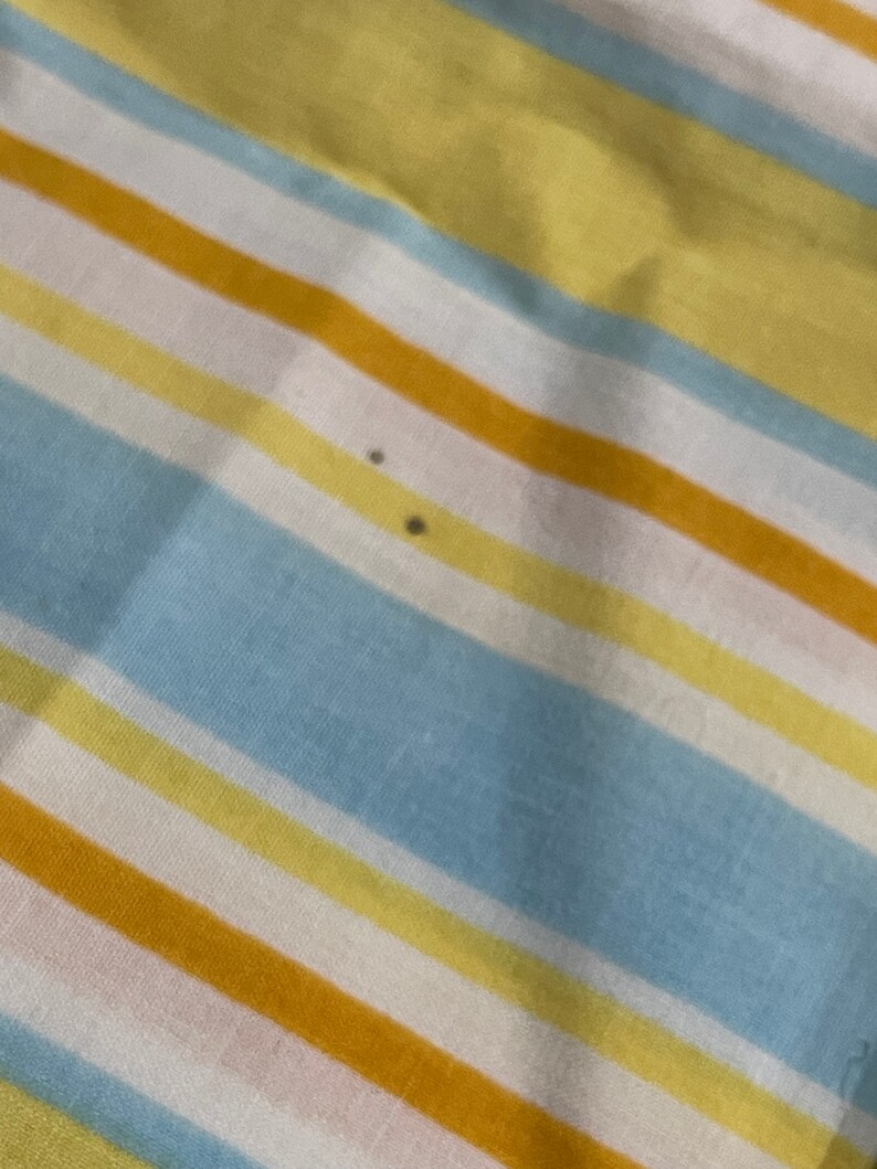 May include: A striped fabric with alternating bands of yellow, light blue, white, and orange. There are two small dark spots on the fabric.