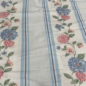 May include: White fabric with blue stripes and a floral pattern. The flowers are pink, blue, and white.