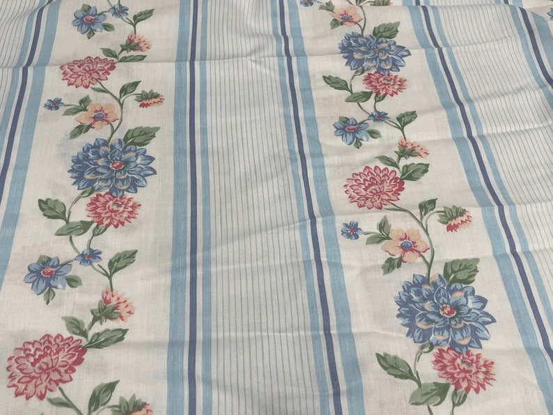 May include: White fabric with blue stripes and a floral pattern. The flowers are pink, blue, and white.